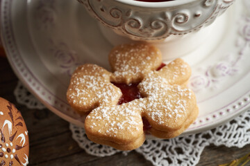 Homemade Linzer cookie in the shape of a four leaf clover near a cup of tea, with Easter egg in the foreground