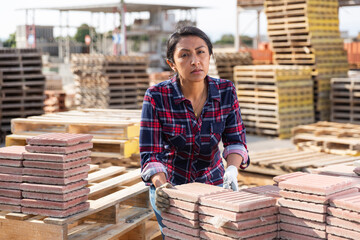 Latin american female supervisor in gloves stacking tiles on pallet at hardware store warehouse