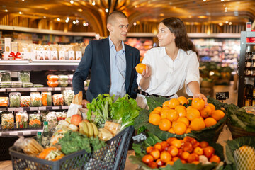 Happy young couple with a grocery cart, who came to the supermarket for shopping, shooses tangerines on the counter