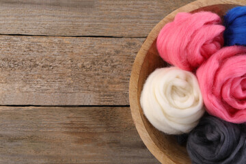 Colorful felting wool in bowl on wooden table, top view. Space for text