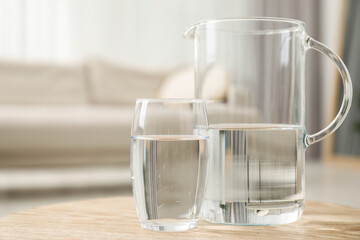 Jug and glass with clear water on wooden table indoors, closeup. Space for text