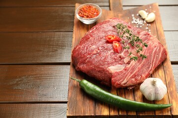 Fresh raw beef cut with spices on wooden table. Space for text
