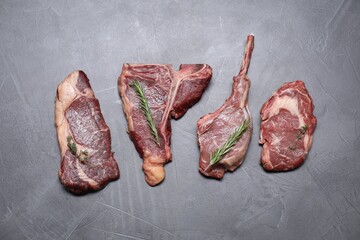 Fresh raw beef cuts with herbs on light grey textured table, flat lay