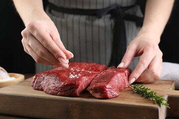 Woman salting fresh raw beef steak at table, closeup