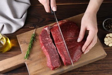 Woman cutting fresh raw beef steak at wooden table, top view