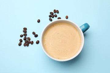 Fresh coffee in cup and roasted beans on light blue background, top view