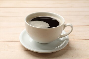 Cup of aromatic coffee on light wooden table, closeup