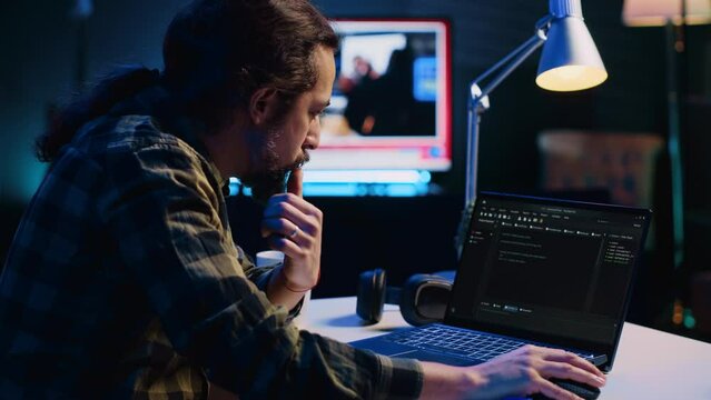 Experienced programmer writes code on laptop screen while in apartment office using Java programming languages. Developer remotely working on fixing database errors while working from home, camera A