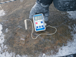 Scientist holding Electronic thermometer measuring volcanic soil temperature with probe stick in...