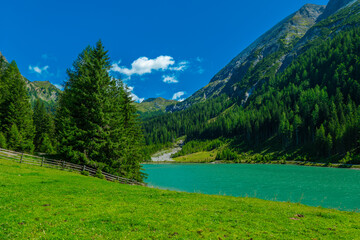 Mountain peak and green transparent water of mountain lake on blue sky with clouds background.Schlierersee, Lungau Austria. Beautiful mountain landscape and lake