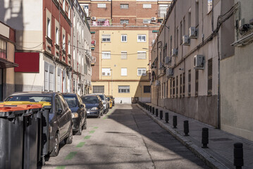 A narrow street with cars parked on one side