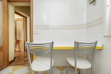 A small white breakfast table with yellow details, a pair of white chairs