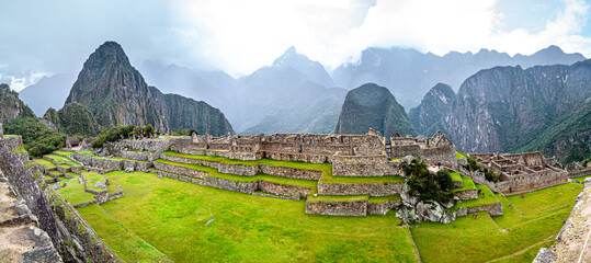A complete scene of Macchu Pichu, in a blue sky day. Many tourists are present and scattered around...
