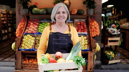 Small business senior woman outside farmer market looking at camera. Latin American owner working at supermarket vegetable store