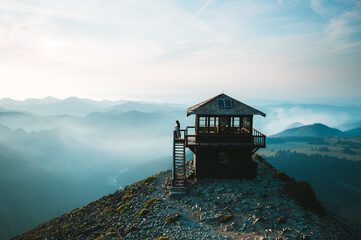 Young woman with blanket on the balcony of fire watch tower enjoying beautiful views of mountains...