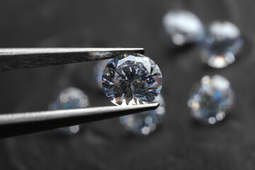 Tweezers with beautiful shiny diamond above dark gray table, closeup