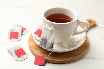 Tea bags and cup of hot beverage on white table, closeup