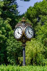 Fototapeta na wymiar Vintage style black and gold metallic clock at the entry in Cismigiu Park, in Bucharest, Romania, in a sunny summer day, vertical picture