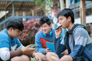 Asian preteen spending freetimes with friends, one of them reading a book and some of them smoking e-cigarettes, bad habit with drug and bad behavior of teens concept