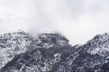 Obraz premium Mountain covered with snow and fog. Alpine landscape in Italy, Europe. Snow-capped mountains against blue sky