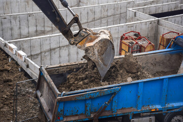 Fototapeta premium Exavator digging and unloading dirt into dump truck at construction site