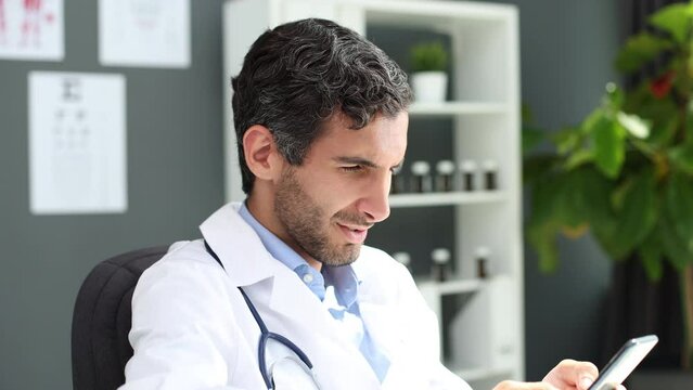 close male doctor in white uniform hold smartphone browse internet in clinic.