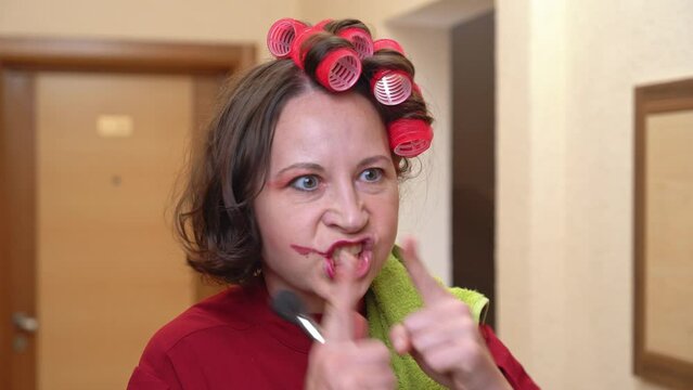 An angry neighbor in curlers emotionally shakes her fingers, scolds for the noise, demands silence, irritably walks away down the corridor Old maid with comical makeup complains, holds back her anger
