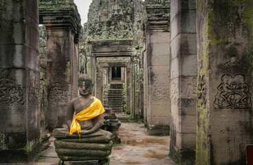 Buddha statue with a yellow scarf along the stone temple building ruins at Bayon Temple. Angkor Wat historical site , Siem Reap, Cambodia 