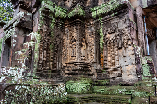 Stone carving detailed pictures on a temple ruin wall and building architecture and moss covered rocks in Ta Prohm Tomb Raider Angkor Wat historical site in Seim Reap Cambodia on a cloudy overcast day