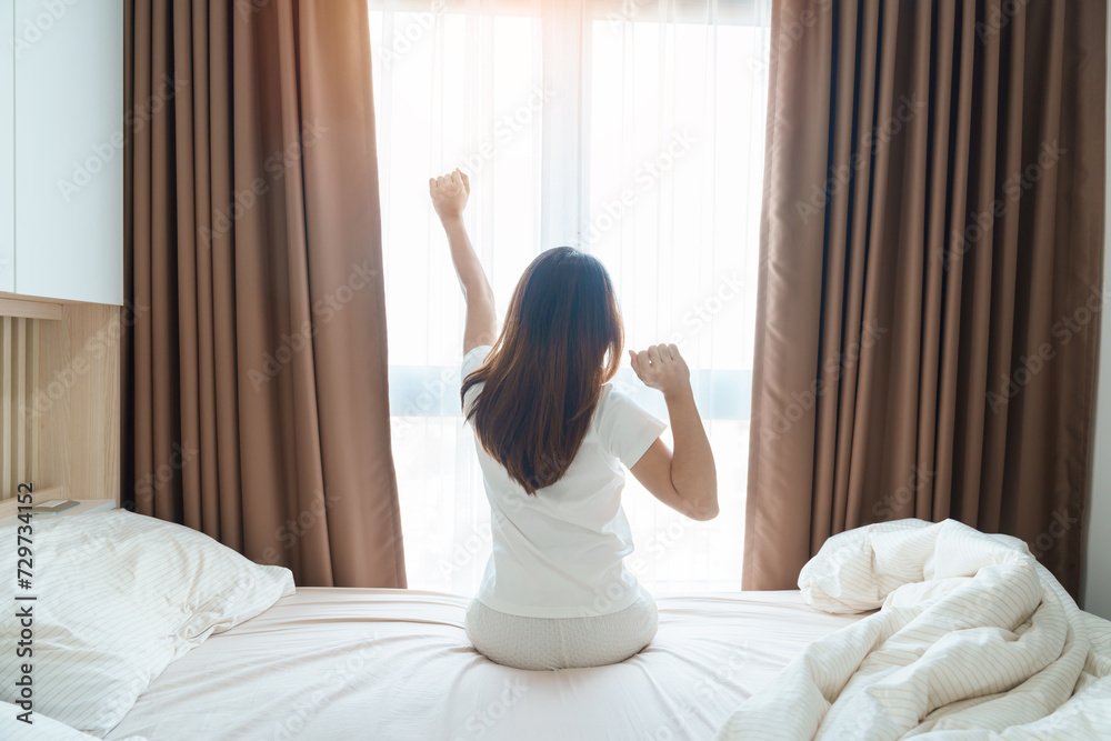Wall mural happy woman stretching on bed after wake up, young adult female rising arms and looking to window in - Wall murals