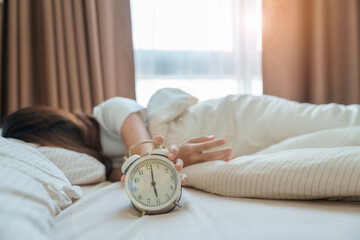 alarm clock and asian woman hand stop time in bed while sleeping, young adult female wake up late...