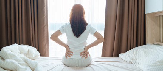 woman having back body ache during sitting on bed at home. adult female with muscle pain after...