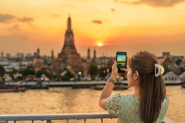 tourist woman enjoys view to Wat Arun Temple in sunset, Traveler take photo to Temple of Dawn by...