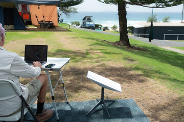 man with satellite internet dish connected working on computer at remote beach side campsite - Powered by Adobe