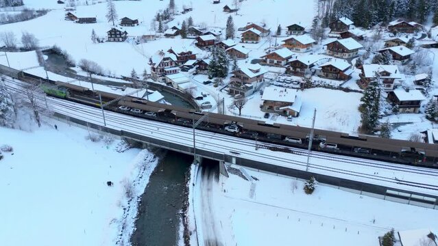Cars driving in car shuttle train in snowy winter town railway station.