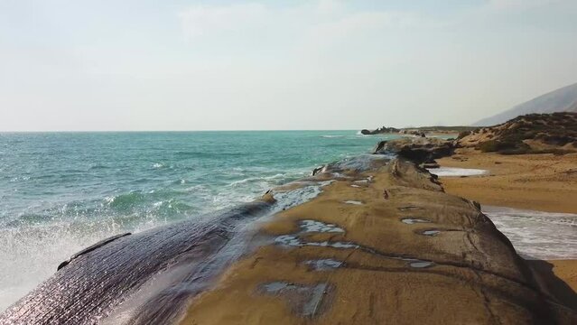 fast moving aerial shot alongside the coast beach erosion in mud dry mountain rock sea wave splash in summer ocean climate in tropical island Hormuz in Iran Qatar border tourist attraction resort hike