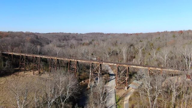 Aerial Shot Pushing Forward Along a Road Towards the Pope Lick Railroad Trestle in Louisville Kentucky, with a Forest in the Background on a Sunny Day.