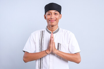 Friendly young Asian muslim man wear skullcap showing greeting gesture with happy expression 
