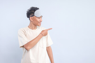 Asian young man with sleep mask pointing aside to the empty space for text or ads