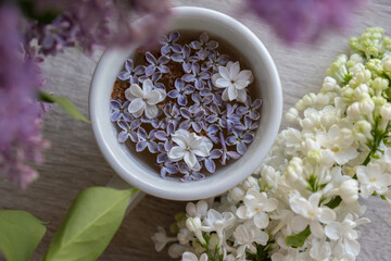 Obraz na płótnie Canvas Tasty black tea in white cup on windowsill with aromatic lilac flowers. Spring composition Cup of lilac tea drinking recipe flowering branches of purple lilac. Still life for copy space greeting card