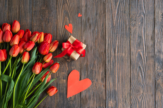 Bouquet of beautiful fresh orange tulips with gift boxe and red paper hearts on wood background. Greeting card with copy space for Valentine's Day, Woman's Day and Mother's Day.