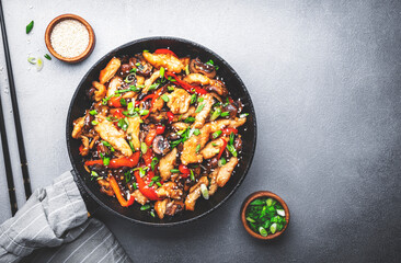 Asian stir fry chicken  slices with red paprika, mushrooms, chives and sesame seeds in frying pan....