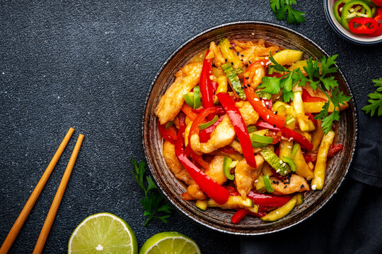 Stir fry turkey breast with red paprika and zucchini with sesame seeds, garlic, ginger and soy sauce in frying pan. Black table background, top view