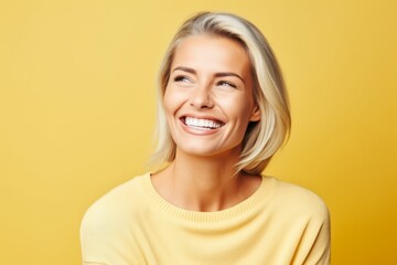 Portrait of happy smiling young blonde woman in yellow sweater over yellow background