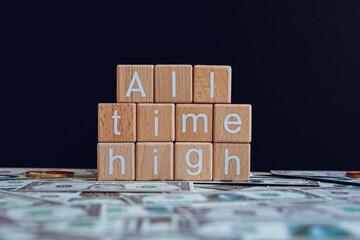 Wooden blocks with the text "All time high" on a black background and crypto banknotes scattered on the ground.