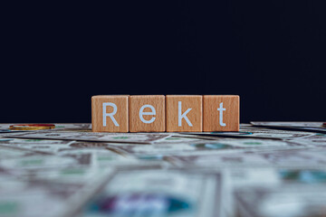 Wooden blocks with the text "Rekt" on a black background and crypto banknotes scattered on the ground.