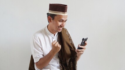asian man with happy expression, playing mobile games, wearing cap and sarong