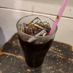 A glass of iced coffee with a pink straw on a wooden table.