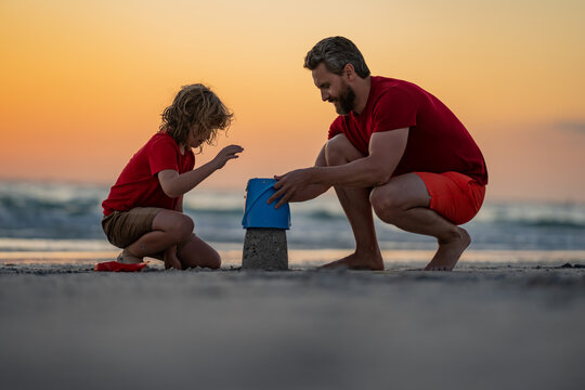 Father and kid son build sand castle at the summer beach, Kid and father building sandcastle. Father and child son playing on the beach. Father and son playing in sand on tropical beach on sunset.