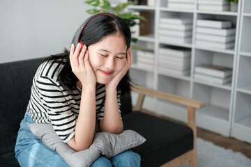 Attractive and happy young Asian woman in casual clothes wearing headphones, relaxes listening to music in her home office.